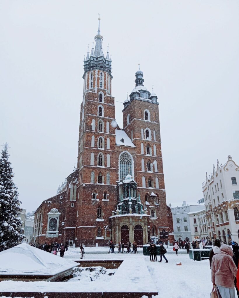 Bazylika Mariacka na Rynku Głównym w Krakowie w padającym śniegu, obok świąteczna choinka