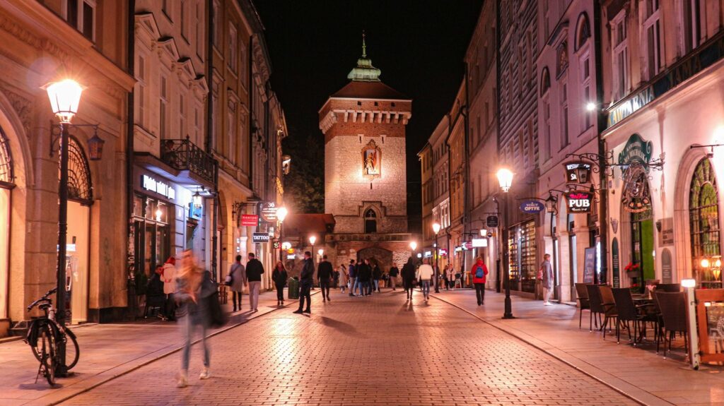 Brama Floriańska w Krakowie nocą, oświetlona ulica Floriańska z nielicznymi przechodniami