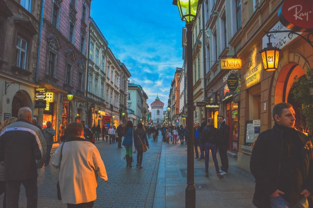 Ulica Floriańska w Krakowie wieczorem: spacerowicze, witryny lokali i latarnie, w głębi Brama Floriańska